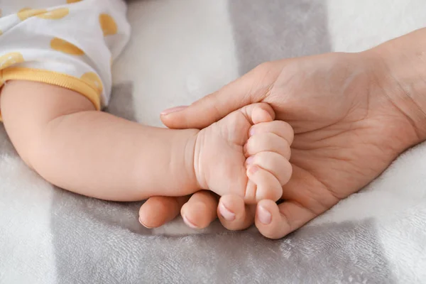 Hands of mother and cute little baby lying on bed, closeup — Stock Photo, Image