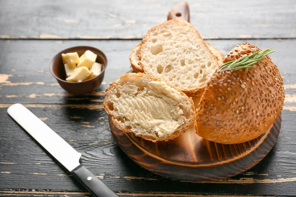 Smakelijke gesneden broodje met boter op donkere houten tafel — Stockfoto