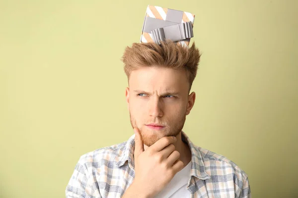 Thoughtful young man with gift box on color background — Stock Photo, Image