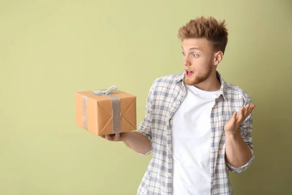 Surprised young man with gift box on color background — Stock Photo, Image