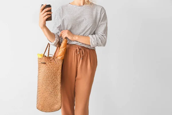 Woman with coffee and products in eco bag on light background — Stock Photo, Image