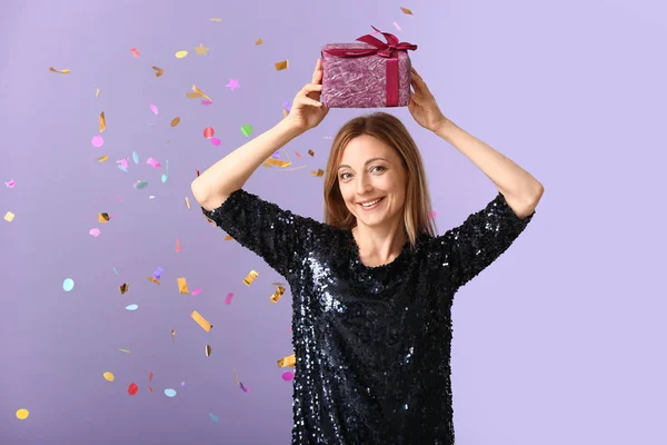 Beautiful woman with gift and falling confetti on color background — Stock Photo, Image