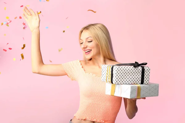 Beautiful young woman with gifts and falling confetti on color background — Stock Photo, Image
