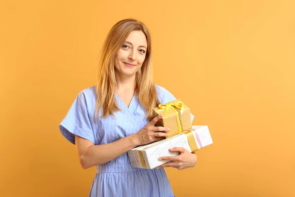 Beautiful woman with gifts on color background — Stock Photo, Image