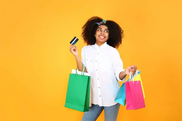 Beautiful African-American woman with shopping bags and credit card on color background — Stock Photo, Image