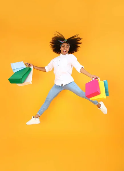Jumping African-American woman with shopping bags on color background — Stock Photo, Image
