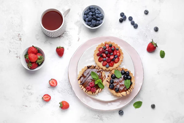 Sweet tartlets with berries and tea on light table — Stock Photo, Image