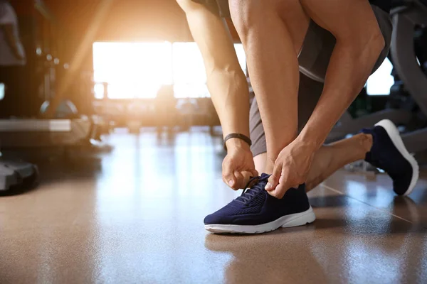 Sporty giovane uomo allacciatura lacci delle scarpe in palestra — Foto Stock