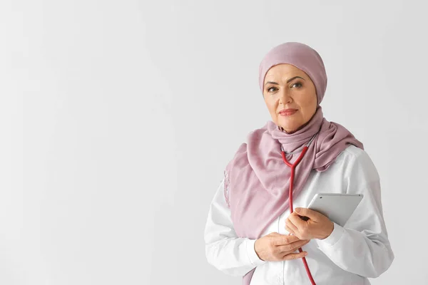 Beautiful mature Muslim doctor with tablet computer on light background — Stock Photo, Image