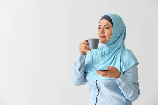 Schöne reife muslimische Frau mit einer Tasse Kaffee auf hellem Hintergrund — Stockfoto