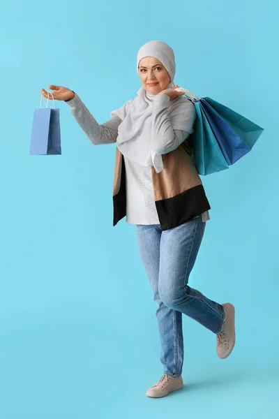 Beautiful mature Muslim woman with shopping bags on color background — Stock Photo, Image