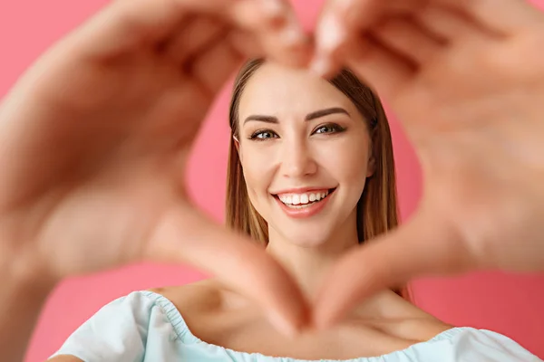 Beautiful young woman making heart with her hands on color background — Stock Photo, Image