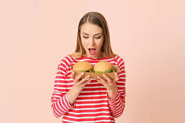 Junge Frau mit leckeren Burgern auf farbigem Hintergrund — Stockfoto