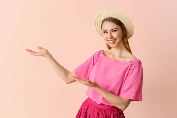 Beautiful young woman showing something on color background — Stock Photo, Image