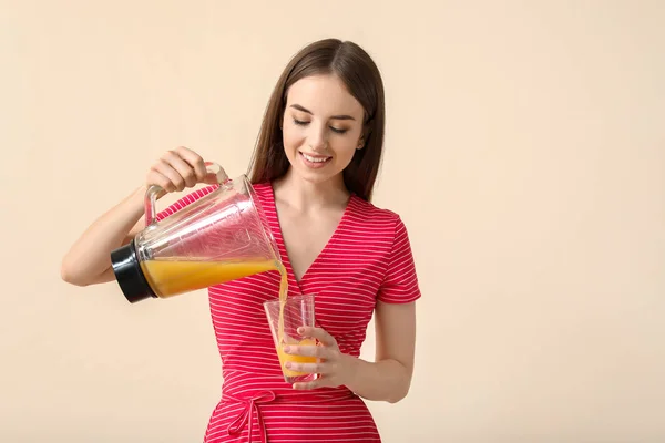 Mujer joven vertiendo jugo saludable de licuadora en vidrio sobre fondo claro —  Fotos de Stock