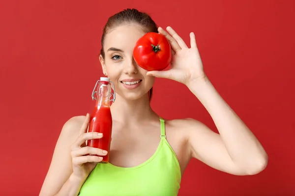 Young sporty woman with healthy juice and fresh tomato on color background