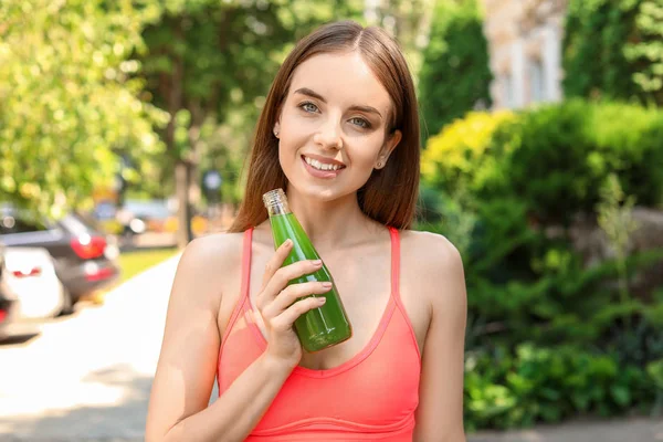 Young sporty woman with healthy vegetable juice outdoors — Stock Photo, Image