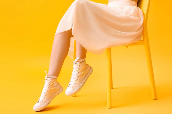 Elegante mujer joven en zapatos y falda sentado en la silla contra el fondo de color —  Fotos de Stock