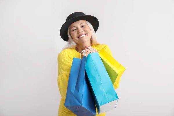 Happy mature woman with shopping bags on light background — Stock Photo, Image