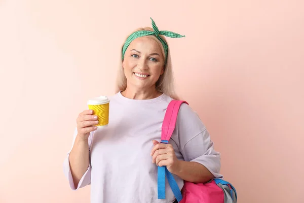 Счастливая зрелая женщина с чашкой кофе и рюкзаком на светлом фоне — стоковое фото