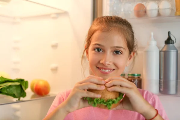 Ragazza mangiare gustoso hamburger vicino frigorifero di notte — Foto Stock