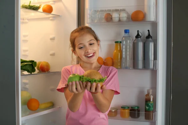 女孩与健康和不健康的食物在冰箱附近在晚上 — 图库照片