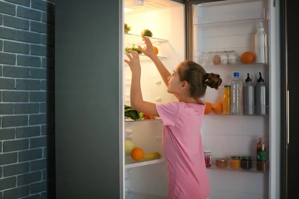 Дівчина вибирає їжу з холодильника пізно вночі — стокове фото