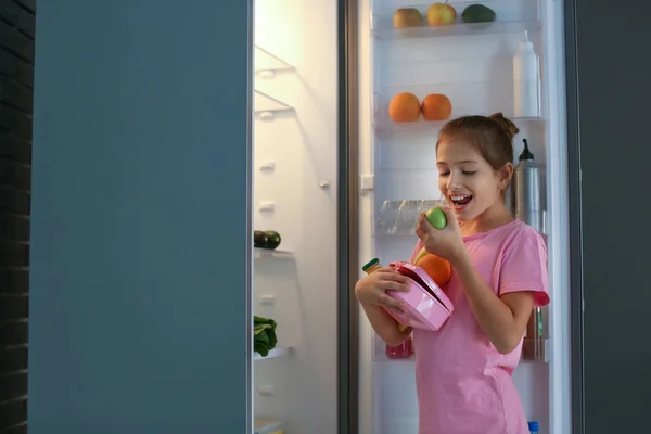 Girl with lot of food near refrigerator at night