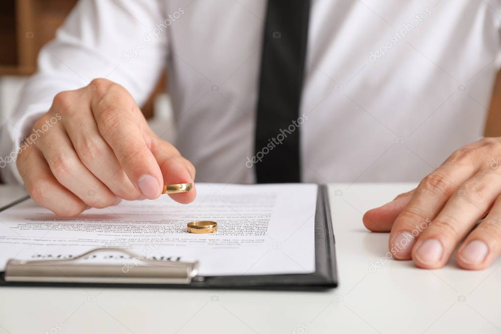 Man with divorce decree and rings sitting at table in lawyer's office, closeup