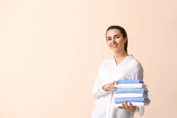 Beautiful young woman with stack of clean towels on light background — Stock Photo, Image