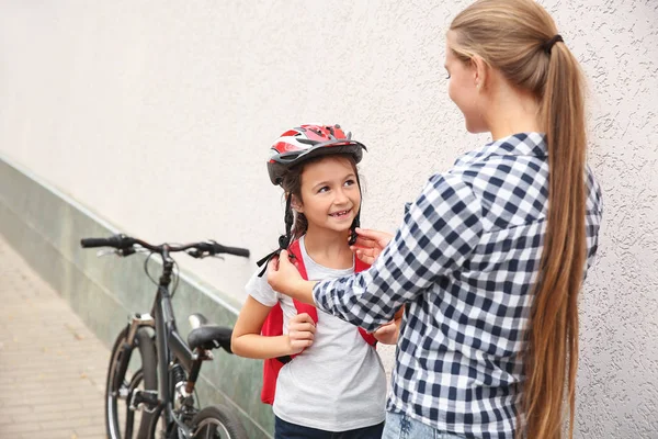 Mother helping her daughter to put on bicycle helmet outdoors — Stock Photo, Image