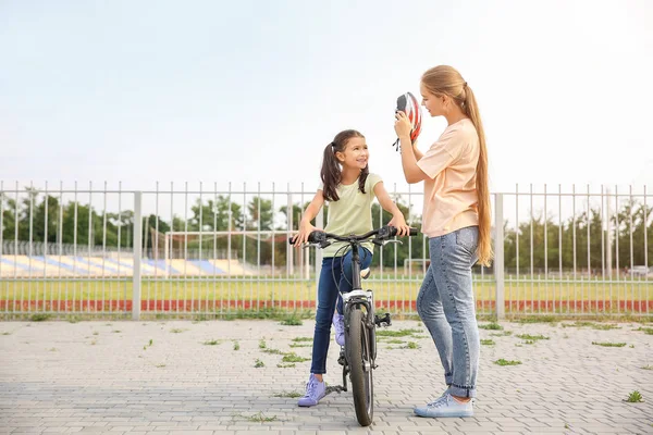 Mother helping her daughter to put on bicycle helmet outdoors — Stock Photo, Image