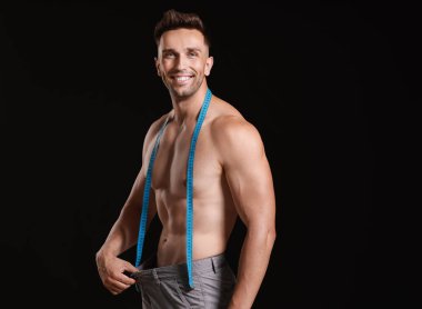 Koyu arkaplanda mezurası olan yakışıklı kaslı adam. Kilo verme konsepti