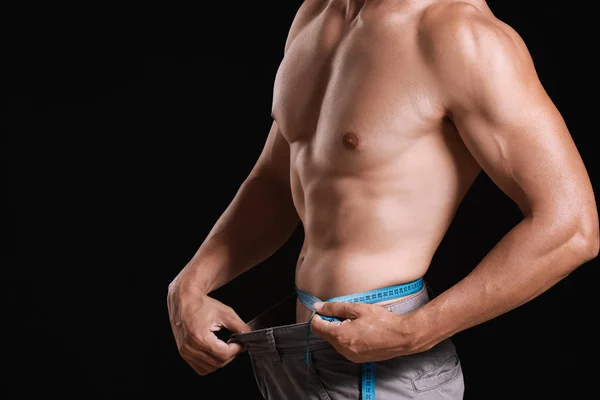 어두운 배경에 줄자 가 있는 근육질의 남자. 체중 감소 개념 — 스톡 사진
