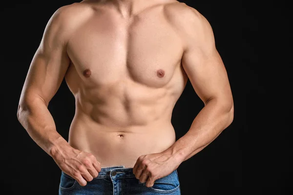 Bonito homem musculoso de jeans soltos em fundo escuro. Conceito de perda de peso — Fotografia de Stock