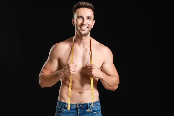 Schöner muskulöser Mann mit Maßband auf dunklem Hintergrund. Konzept zur Gewichtsreduktion — Stockfoto