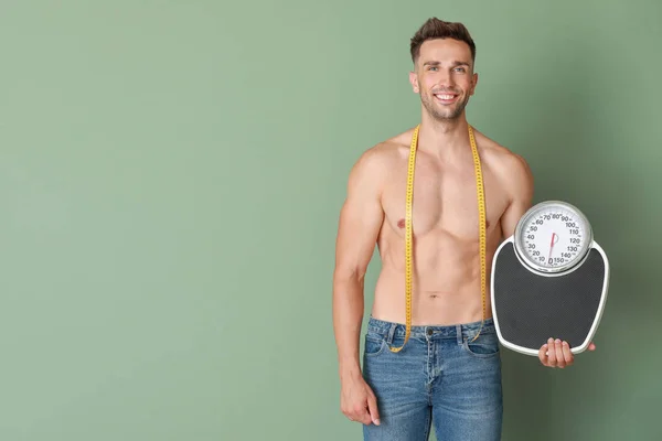 Handsome muscular man with measuring tape and scales on color background. Weight loss concept — Stock Photo, Image