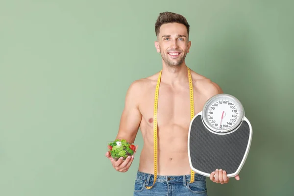 Handsome muscular man with measuring tape, scales and salad on color background. Weight loss concept — Stock Photo, Image