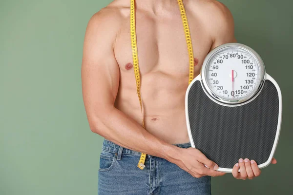 Handsome muscular man with measuring tape and scales on color background. Weight loss concept — Stock Photo, Image