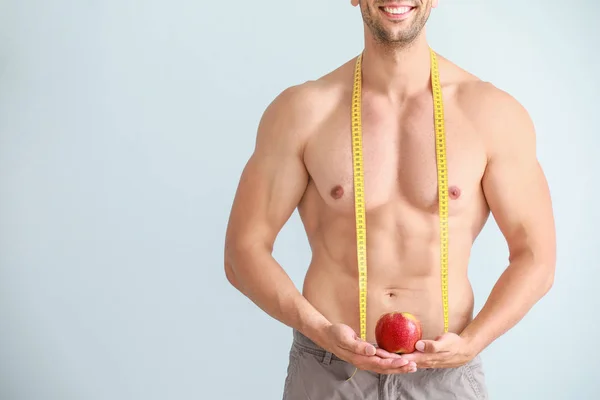 Handsome muscular man with measuring tape and apple on color background. Weight loss concept — Stock Photo, Image