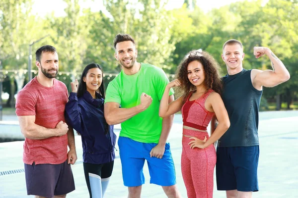 Groep jonge sportieve mensen die spieren buitenshuis tonen — Stockfoto