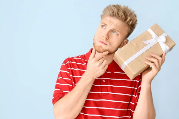 Thoughtful young man with gift box on color background