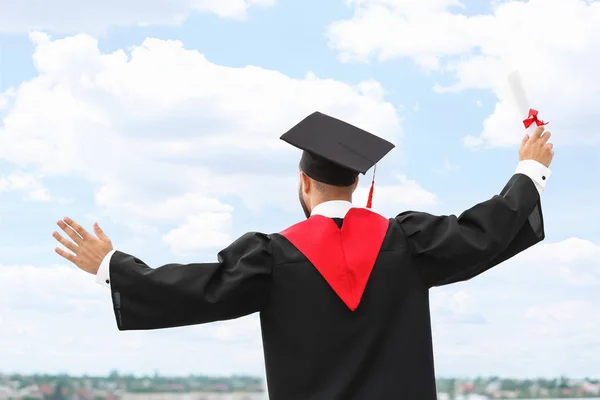 Gelukkige student in Bachelor gewaad en met diploma buitenshuis — Stockfoto