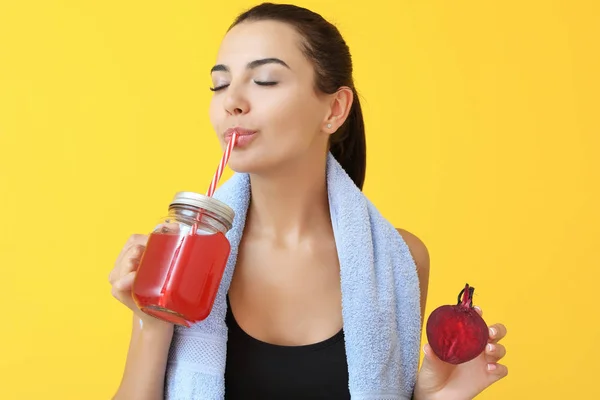 Young sporty woman drinking healthy beet juice on color background — Stock Photo, Image