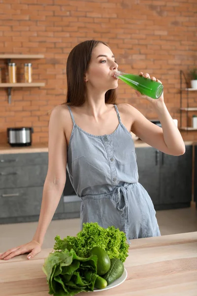 Young woman drinking healthy vegetable juice in kitchen — Stock Photo, Image