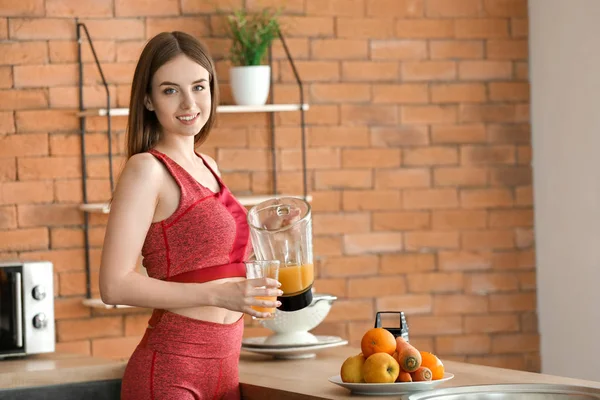 Jovem mulher esportiva preparando suco de legumes saudável na cozinha — Fotografia de Stock