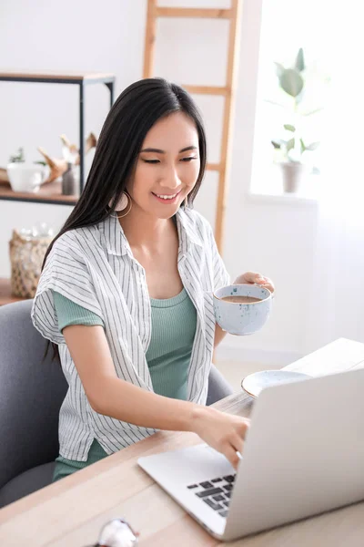 Asian blogger with laptop drinking coffee at table — Stock Photo, Image