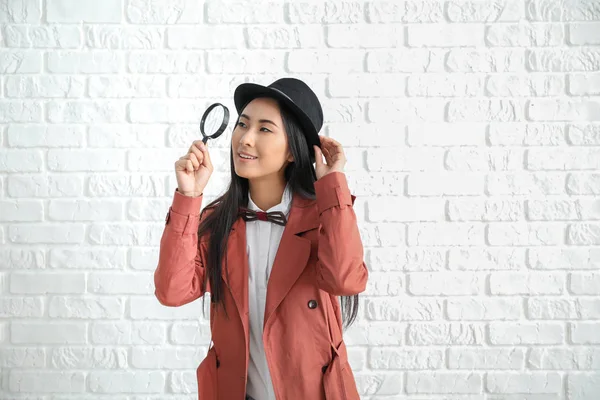 Female Asian detective with magnifying glass against white brick wall