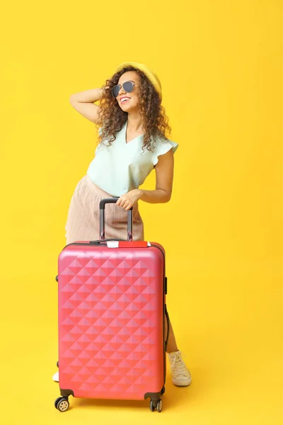 Stylish African-American woman with luggage on color background — Stock Photo, Image