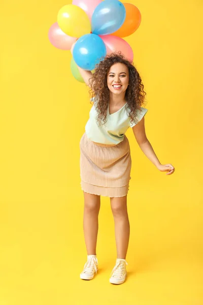 Happy African-American woman with air balloons on color background — Stock Photo, Image